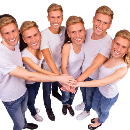Group of six men with blonde hair wearing cardboard face masks white shirts and jeans, standing in a circle with hands stacked on top of each other against a white background.